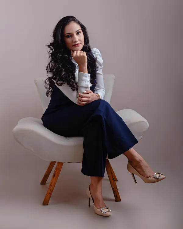 Déborah Aquino sentada em uma poltrona, em retrato profissional